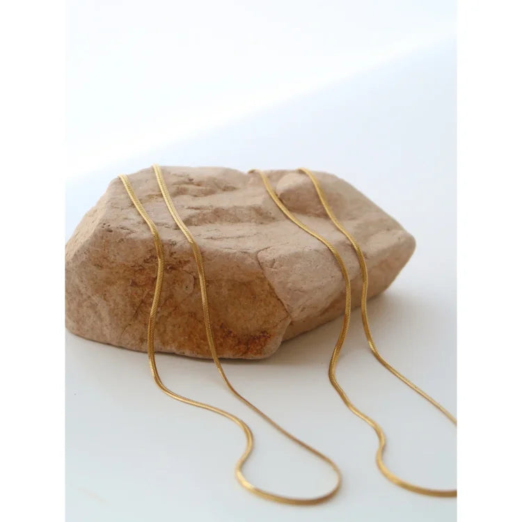 Goldene Schlangenkette auf Stein, elegantes Schmuckdesign, minimalistisch, modisch, Damenaccessoire.
