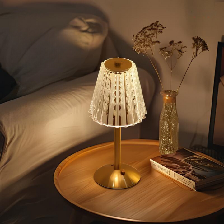 Goldene Tischlampe mit gemustertem Schirm auf Holztisch, gemütliche Beleuchtung im Schlafzimmer.