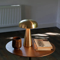 Goldene Tischlampe aus Metall auf Holztisch mit Keramikbecher und Büchern, modernes Design.
