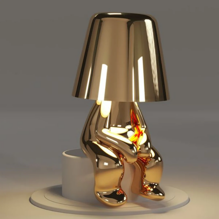Goldene Designer-Tischlampe in Form einer sitzenden Figur, modernes Wohnaccessoire.