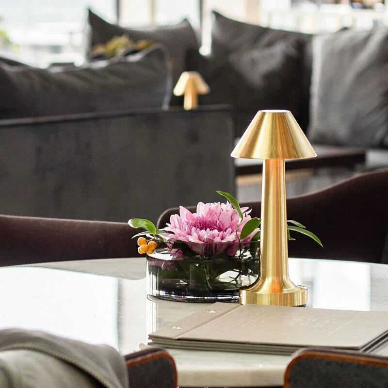 Goldene Tischlampe aus Metall neben rosa Blume auf modernem Wohnzimmertisch.