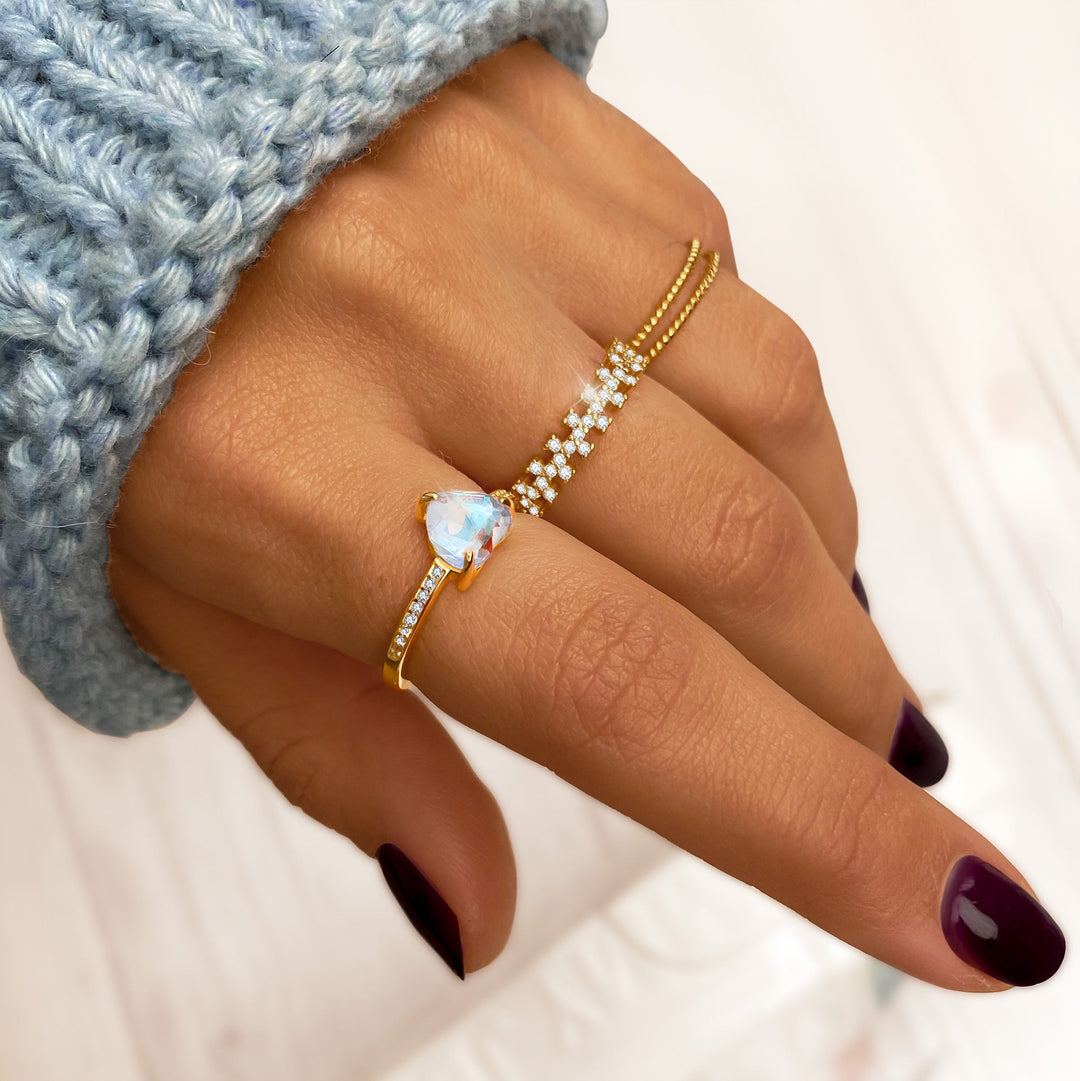 Hand mit goldenen Ringen, Opal und Diamanten, gestrickter blauer Pullover, elegante Maniküre.