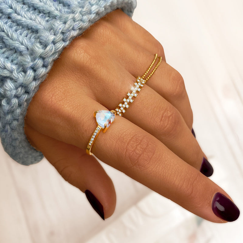 Hand mit goldenen Ringen, Opal und Diamanten, gestrickter blauer Pullover, elegante Maniküre.