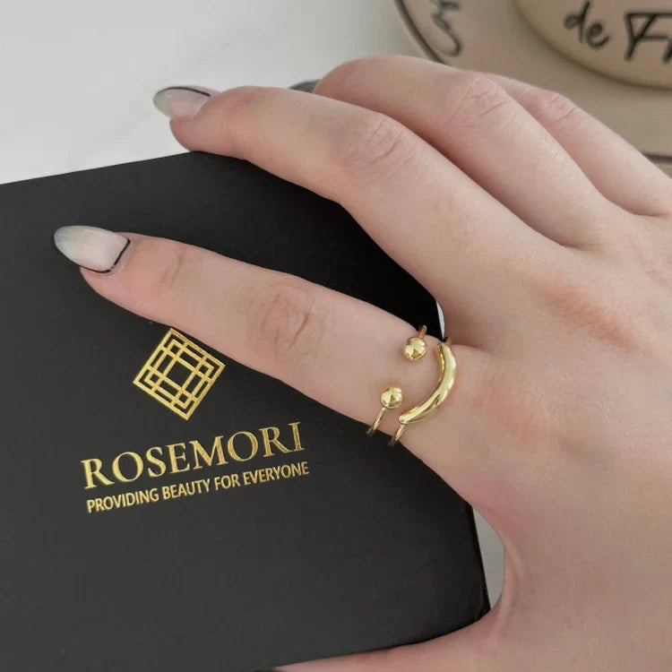 Goldener offener Ring mit Kugeldetails auf Hand, Rosemori-Schmuckschachtel im Hintergrund.