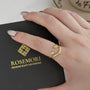 Goldener offener Ring mit Kugeldetails auf Hand, Rosemori-Schmuckschachtel im Hintergrund.