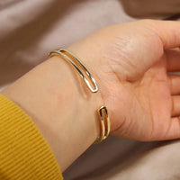 Goldenes Armreif-Armband auf Handgelenk, minimalistisches Design, eleganter Schmuck.