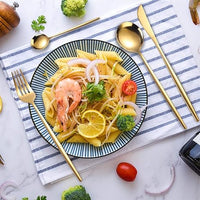 Pasta mit Garnelen, Zitrone, Brokkoli auf gestreiftem Tuch, goldfarbenes Besteck, Tomate.