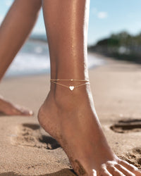 Goldenes Fußkettchen mit Herzanhänger am Strand, Schmuck für Damen, Sommermode Accessoire.