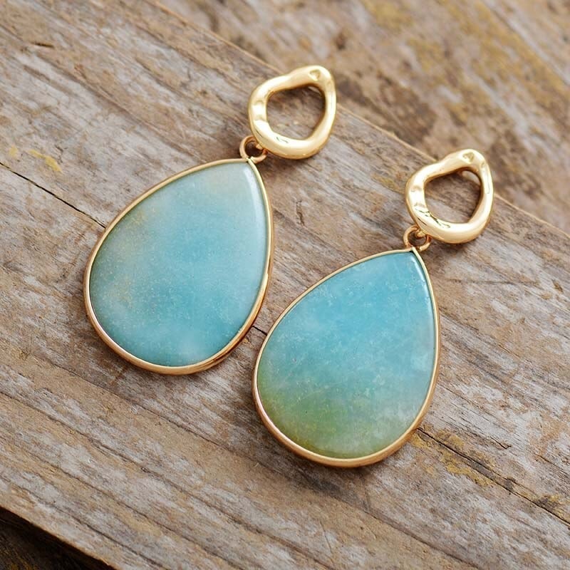 Blaue Tropfen-Ohrringe mit goldener Fassung auf Holz, eleganter Schmuck für Damen.