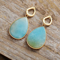 Blaue Tropfen-Ohrringe mit goldener Fassung auf Holz, eleganter Schmuck für Damen.