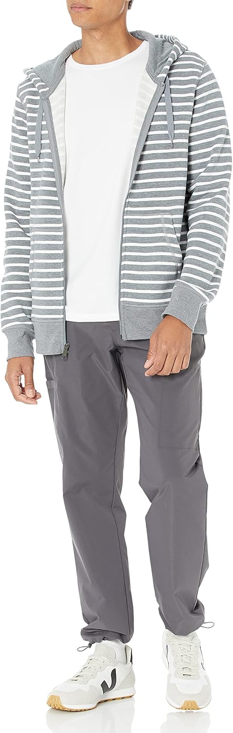 Mann in grauer gestreifter Kapuzenjacke, weißem T-Shirt, grauer Hose und weißen Sneakers.