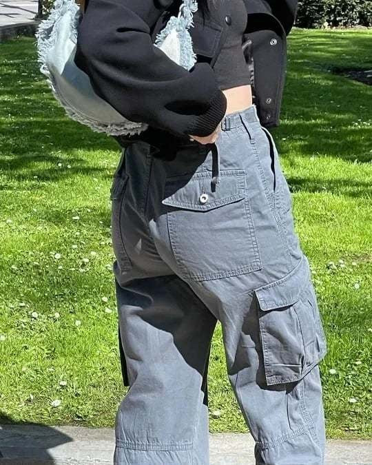 Frau in grauer Cargo-Hose und schwarzer Jacke im Park, modisch, Freizeitkleidung.