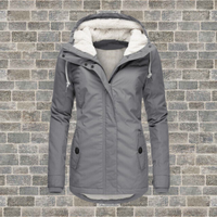 Graue Damen-Winterjacke mit Kapuze, Fleece-Futter, Reißverschluss, vor Ziegelwand.