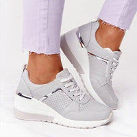 Graue Damen-Sneaker mit Keilabsatz, perforiertem Design und silbernen Akzenten.