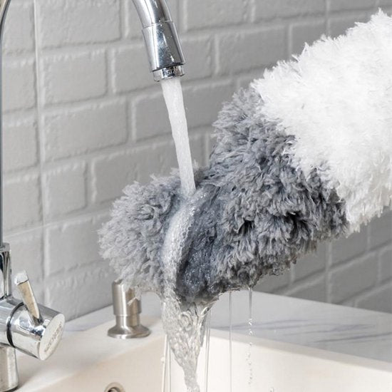 Grauer, flauschiger Reinigungshandschuh unter Wasserhahn, Badezimmer, weiße Fliesenwand.