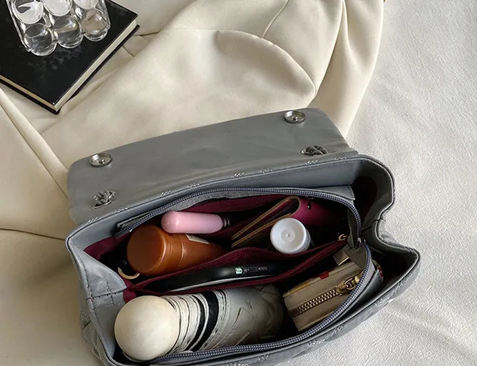 Graue Handtasche mit Kosmetik, Geldbörse und Notizbuch auf beigem Stoff.