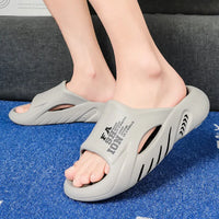 Graue Unisex-Badeschlappen, rutschfest, bequem, mit Schriftzug, auf blauem Teppich.