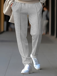 Graue Damenhose aus Baumwolle, elegant, mit Bügelfalten, kombiniert mit weißen Sneakers.