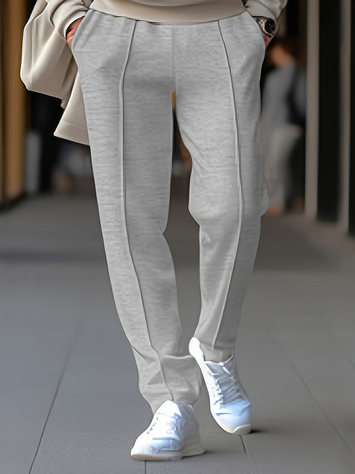 Graue Damenhose aus Baumwolle, elegant, mit Bügelfalten, kombiniert mit weißen Sneakers.