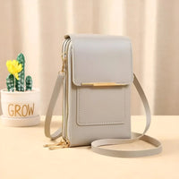 Graue Leder-Umhängetasche mit goldenen Reißverschlüssen, neben Kaktus im Topf.