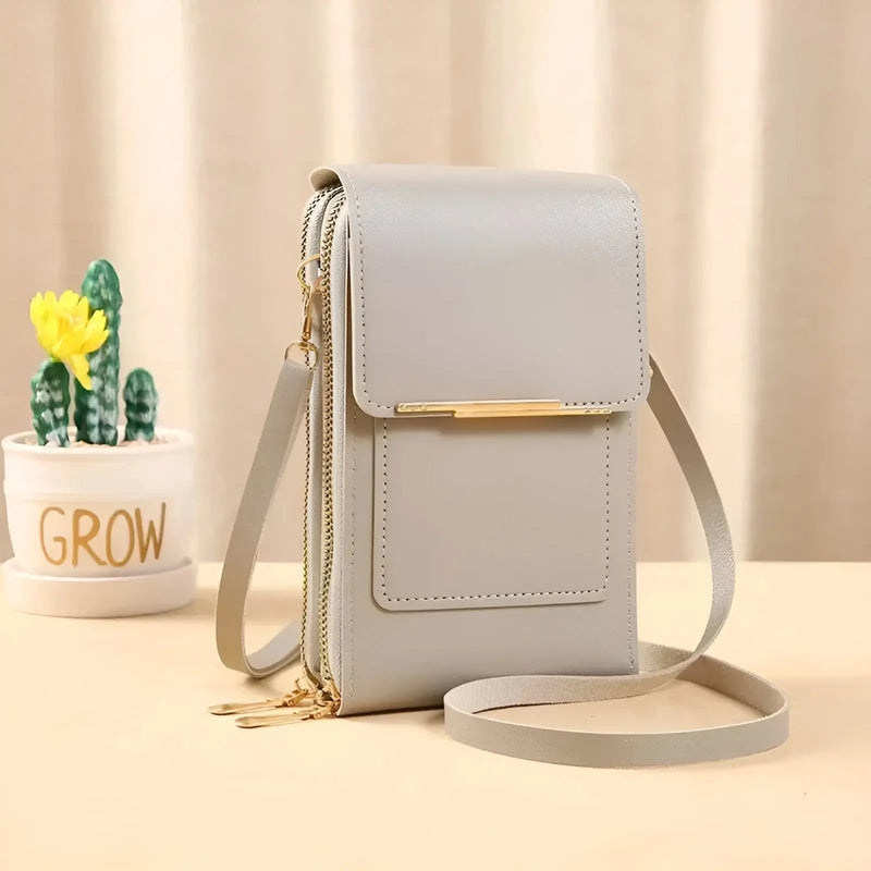 Graue Leder-Umhängetasche mit goldenen Reißverschlüssen, neben Kaktus im Topf.