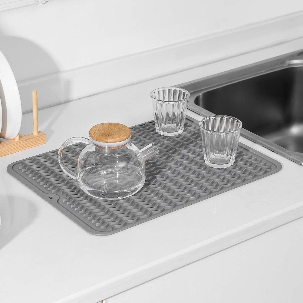 Graue Silikon-Abtropfmatte neben Spüle mit Gläsern und Teekanne, rutschfest, hitzebeständig.