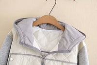 Graue Kapuzenjacke mit Reißverschluss, gesteppte Vorderseite, hängend auf Holzkleiderbügel.