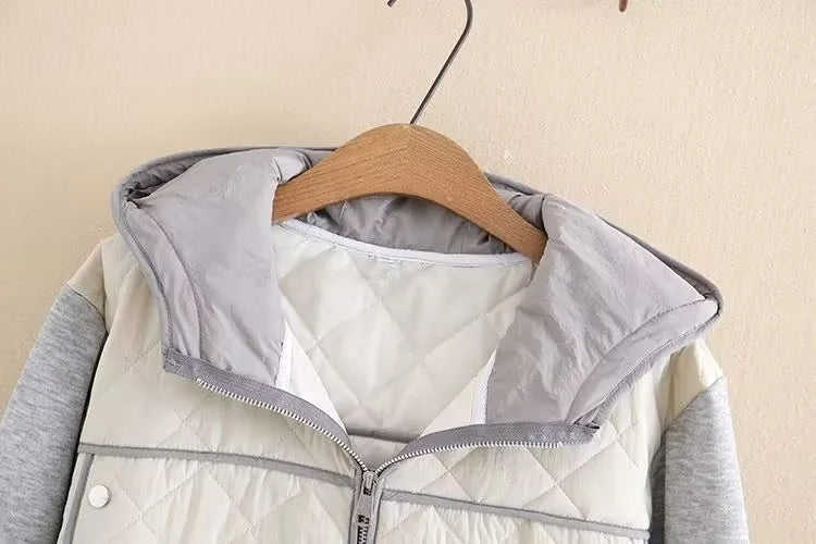 Graue Kapuzenjacke mit Reißverschluss, gesteppte Vorderseite, hängend auf Holzkleiderbügel.