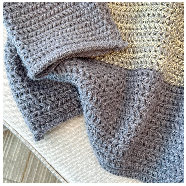 Graue Strickdecke aus Wolle auf beigem Sofa, gemütlich und warm, ideal für Wohnzimmer.