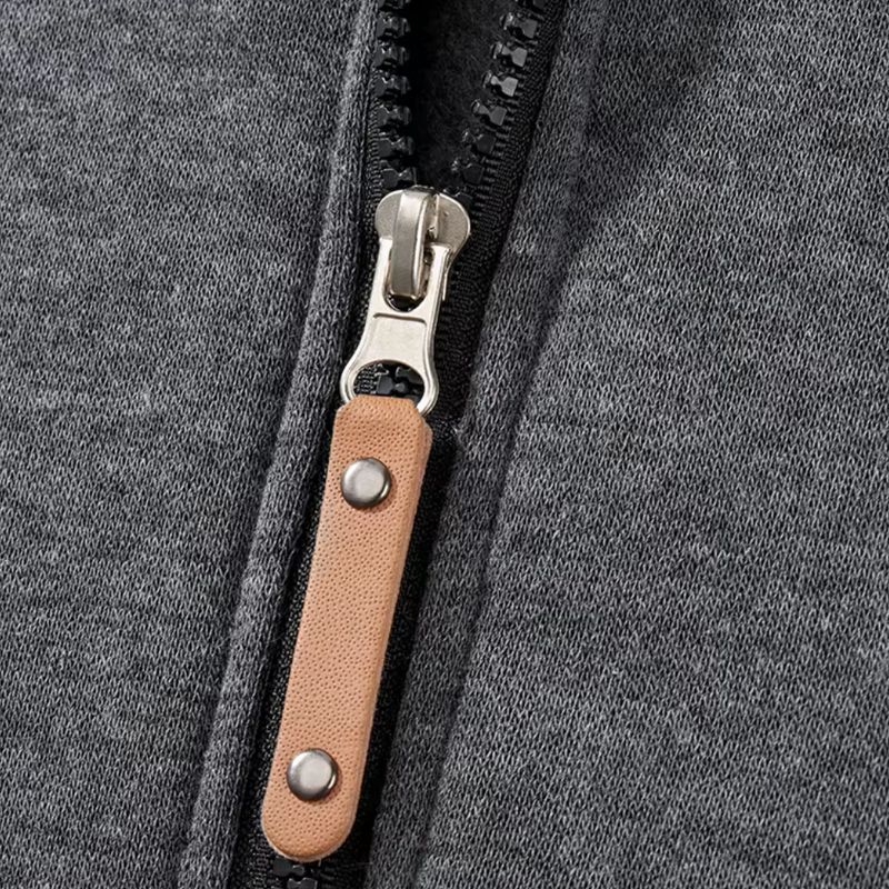 Grauer Hoodie mit Reißverschluss, Metallzipper und braunem Lederzug, Nahaufnahme.
