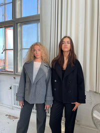 Zwei Frauen in grauem und schwarzem Blazer, moderne Mode, urbaner Stil, helle Umgebung.