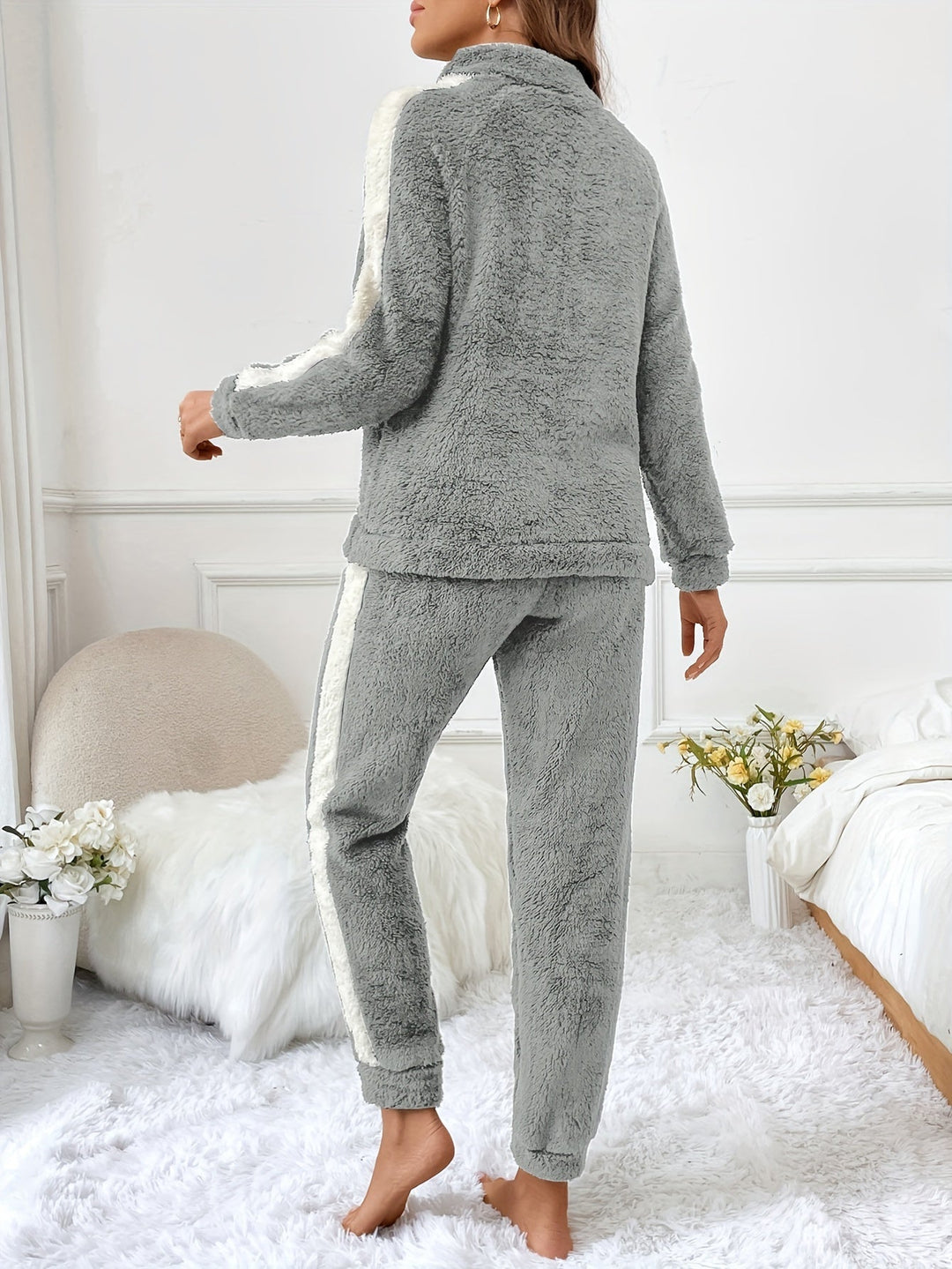 Frau in grauem Fleece-Pyjama-Set, gemütlich, modisch, Schlafzimmer, Blumen, Rückansicht.