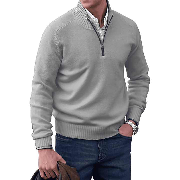 Mann in grauem Pullover mit Reißverschluss, Hemd und Jeans, hält braune Jacke, modisch, lässig.