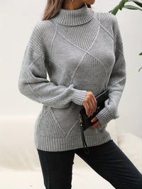 Frau in grauem Strickpullover mit Rollkragen, hält schwarze Clutch, modisch, elegant.