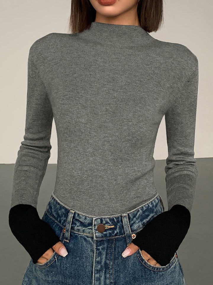 Frau in grauem Rollkragenpullover und blauen Jeans mit schwarzen Ärmelabschlüssen.