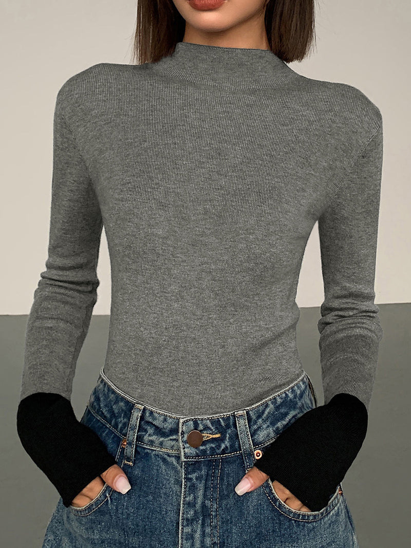 Frau in grauem Rollkragenpullover und blauen Jeans mit schwarzen Ärmelabschlüssen.