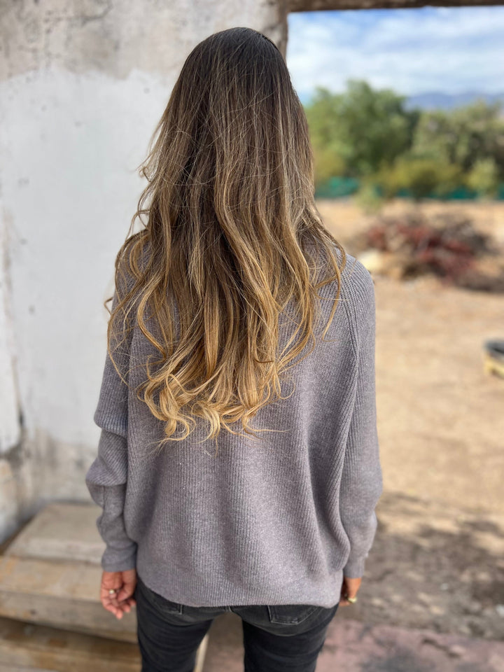 Frau in grauem V-Ausschnitt-Pullover, lange Ärmel, draußen, Rückansicht.