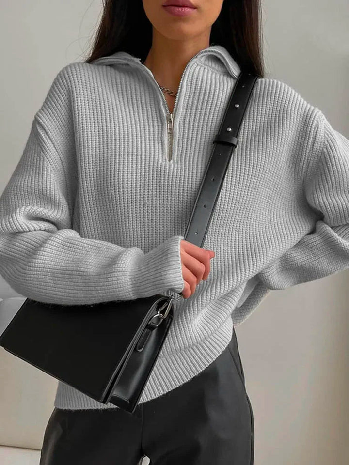 Frau in grauem Strickpullover mit V-Ausschnitt und schwarzer Ledertasche, modisch, elegant.