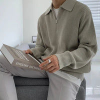 Mann in grauem Strickpullover hält englisches Wörterbuch, sitzt auf grauem Sofa.