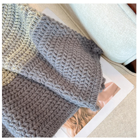 Grauer Strickschal aus Wolle auf beigem Sofa, gemütlich, warm, modisch, Winteraccessoire.