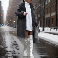 Frau in grauem Mantel und weißen Stiefeln auf verschneiter Stadtstraße im Winter.