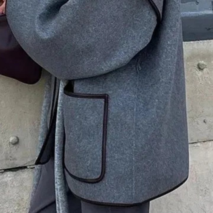 Grauer Wollmantel mit schwarzer Paspelierung, große Tasche, elegantes Design.