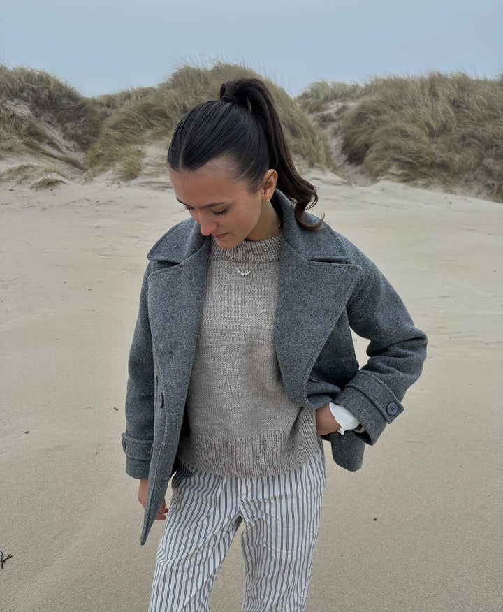Frau im grauen Wollmantel am Strand, gestreifte Hose, lässige Mode, Herbstoutfit.