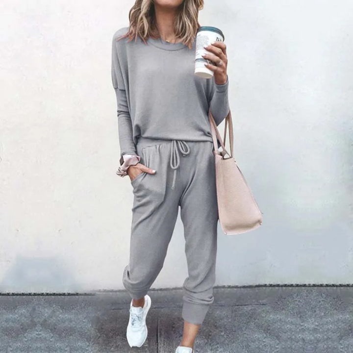 Frau in grauem Jogginganzug mit Kaffeebecher und rosa Tasche, lässige Mode, Straßenstil.