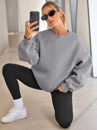 Frau in grauem Oversize-Pullover, schwarzen Leggings, Sonnenbrille, macht Selfie, sportlich.