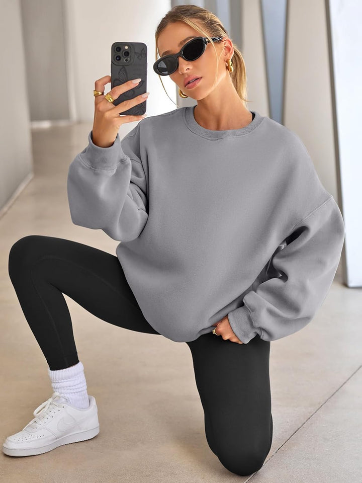 Frau in grauem Oversize-Pullover, schwarzen Leggings, Sonnenbrille, macht Selfie, sportlich.