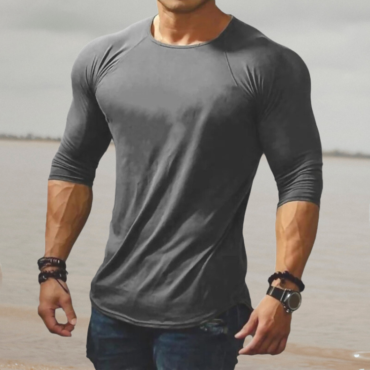 Mann in grauem, enganliegendem Langarmshirt am Strand, muskulös, modisch, Freizeitkleidung.