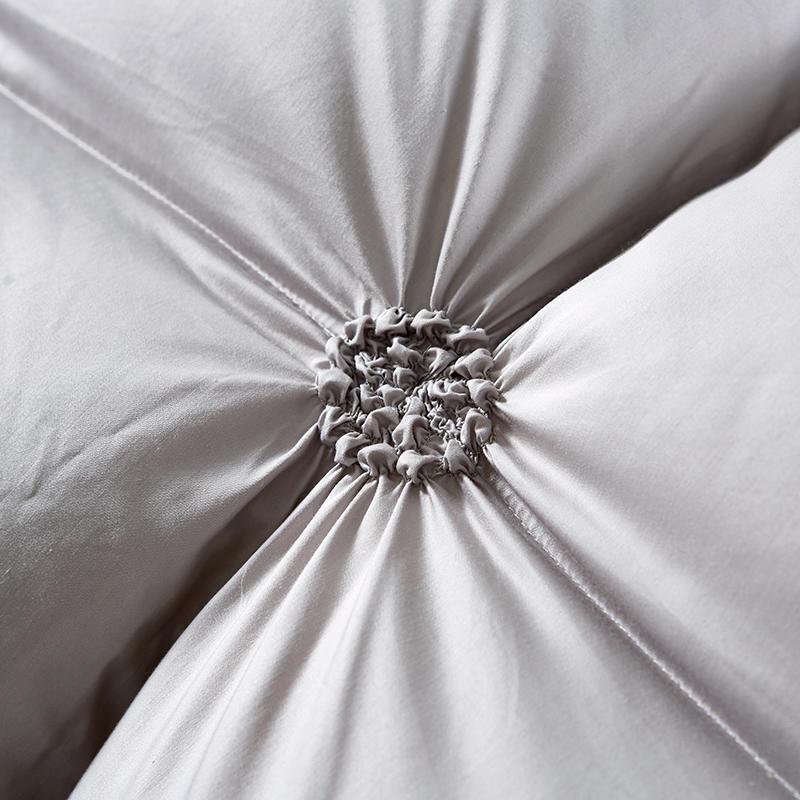 Nahaufnahme graues Baumwollkissen mit dekorativer Raffung, weiches Wohnaccessoire, Schlafzimmerdekor.