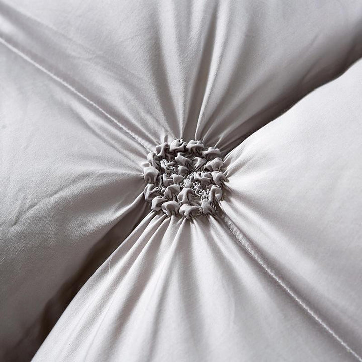 Nahaufnahme graues Baumwollkissen mit dekorativer Raffung, weiches Wohnaccessoire, Schlafzimmerdekor.