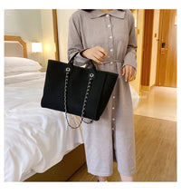 Frau in grauem Kleid mit schwarzer Handtasche aus Leder und Kette im Hotelzimmer.